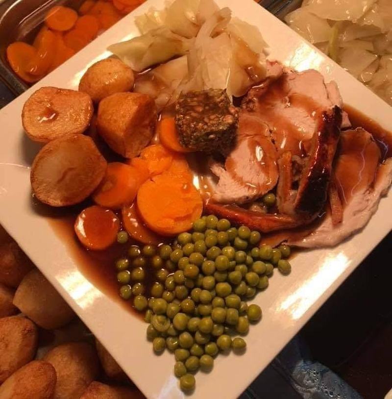 A finished roast dinner plate with turkey, roast potatoes, carrots, peas, cabbage and gravy